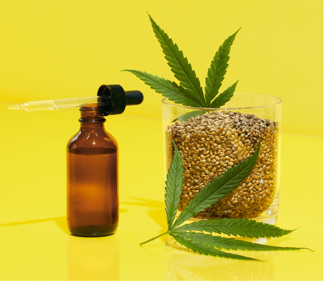 Hemp seed oil in a bottle with dropper next to jar of hemp seeds with hemp leaves